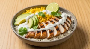 A beautifully presented, vibrant close-up of a Grilled Chicken Bowl with Avocado and Corn, topped with fresh cilantro and a lime wedge, ready to be enjoyed.